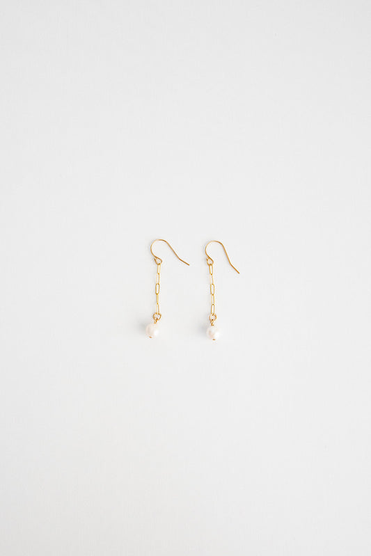 A pair of freshwater pearl earrings hung on a 14k gold chain and shepherd's hook lay on a white flatlay background.