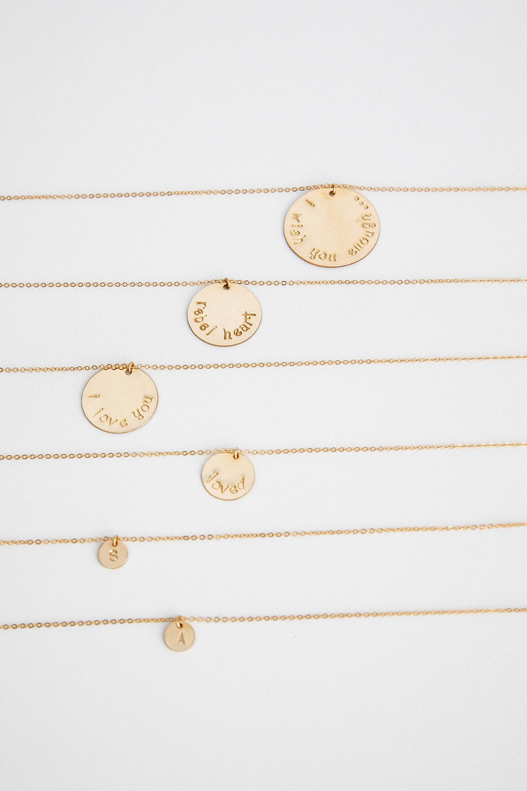 Six 14k gold filled chain necklaces with 14k gold filled discs with hand stamped letters laying on a white background. 