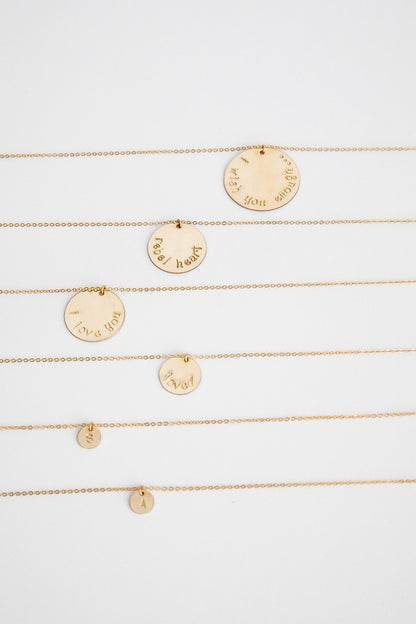 14k gold filled chain necklaces with 14k gold filled hand stamped disc lay on a white background. The discs read "I wish you enough", "rebel heart", "I love you", "loved", "S", and "A".