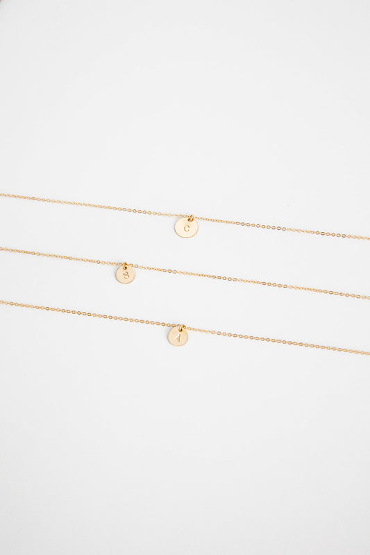 Three 9.5mm 14k gold filled necklaces with hand stamped single letter 14k gold discs lay on a white background.