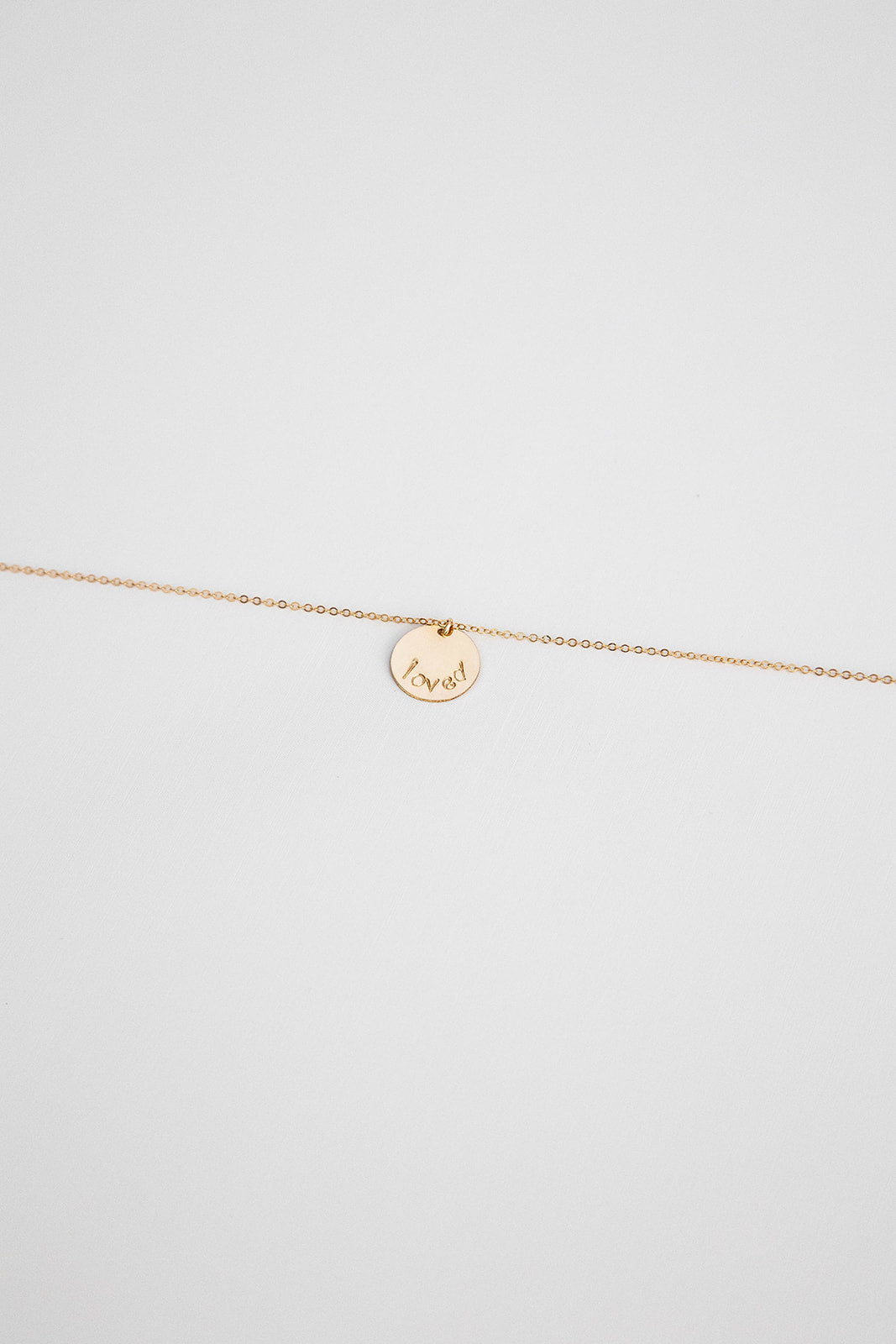 A 14k gold filled disc hung on a 14k gold chain necklace with the word "loved" hand stamped on the disc.