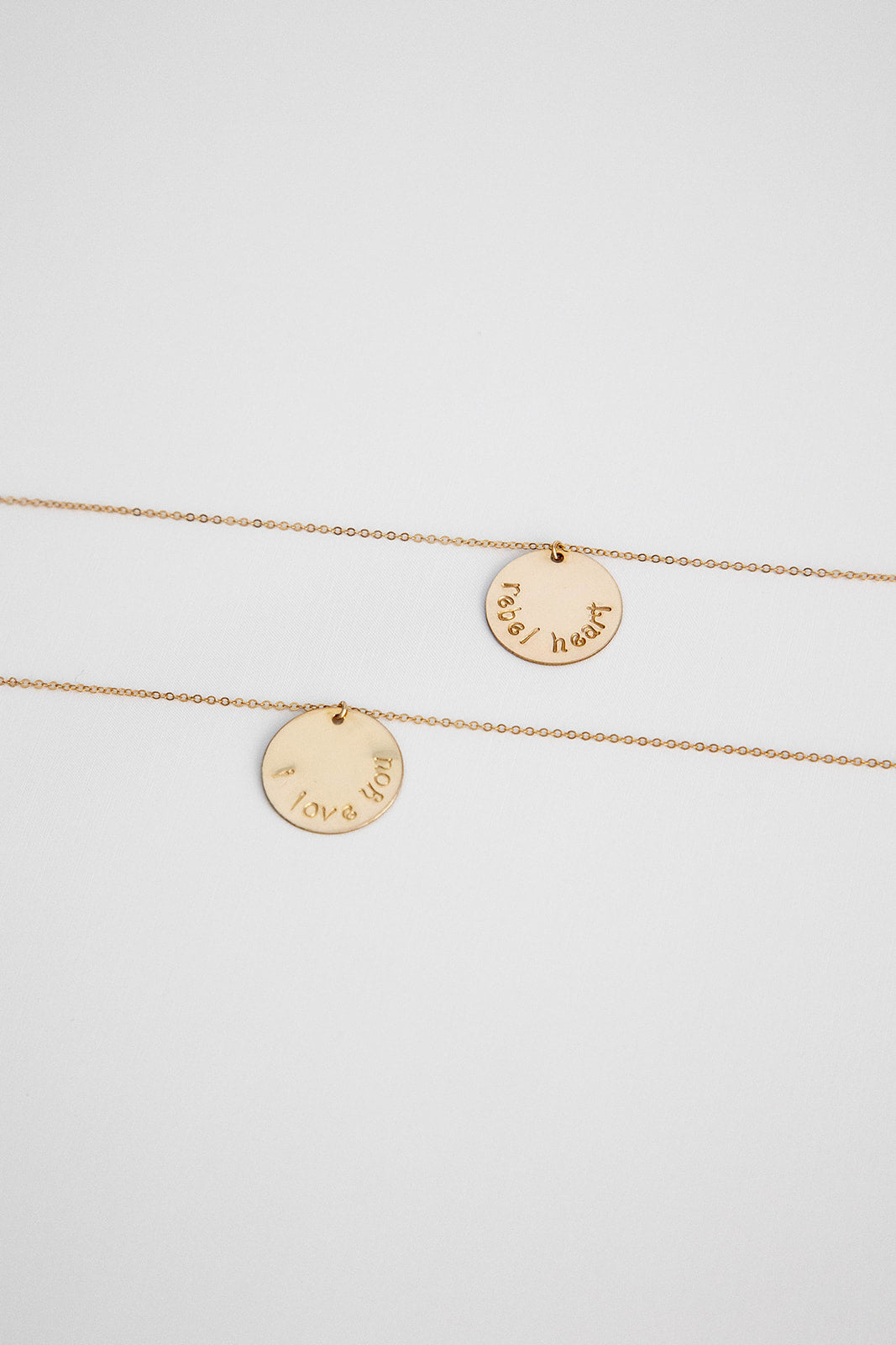 Two 14k gold filled cable link chain necklaces with 19.1mm 14k gold hand stamped disc lay on a white background flatlay.