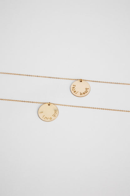 Two 14k gold filled cable link chain necklaces with 19.1mm 14k gold hand stamped disc lay on a white background flatlay.