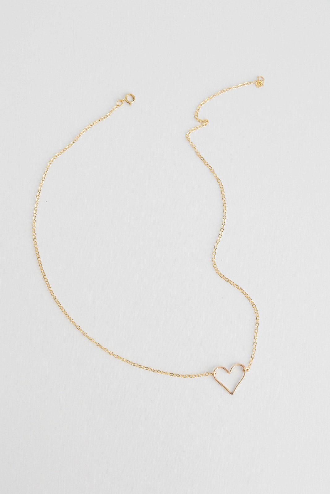 A dainty 14k gold filled floating heart necklace laying on a white background.