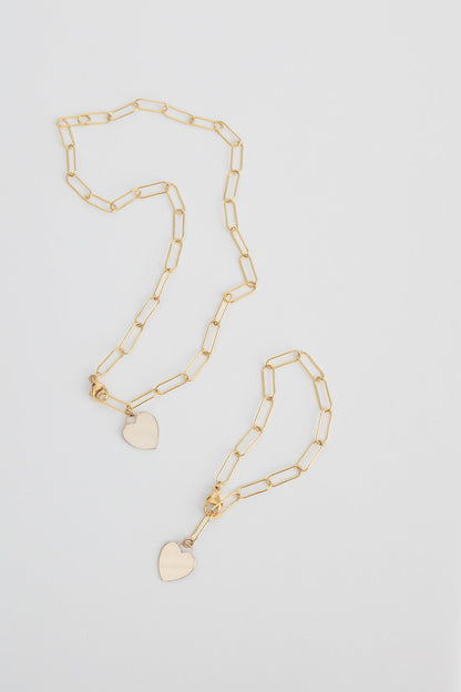 A lightweight 14k gold filled paper clip chain necklace with 14k gold filled heart charm lays on a white background with a matching bracelet next to it.