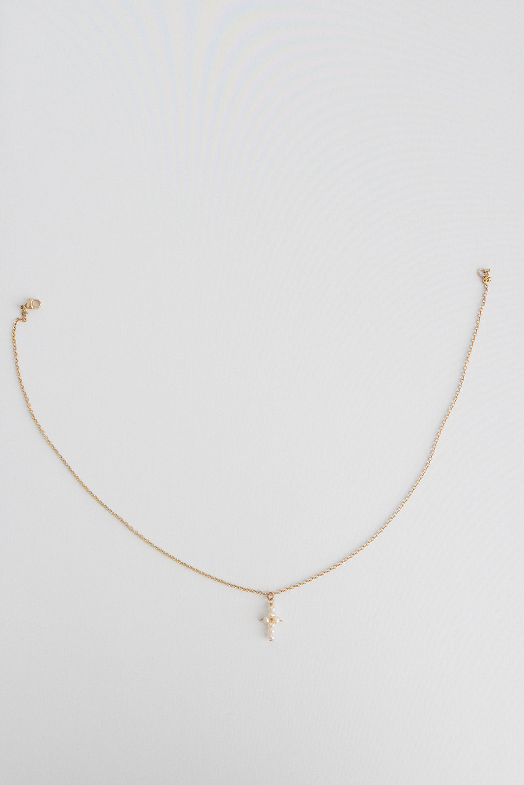 A 14k gold filled cable link chain necklace with freshwater pearls connected in the shape of a cross lays on a white background.