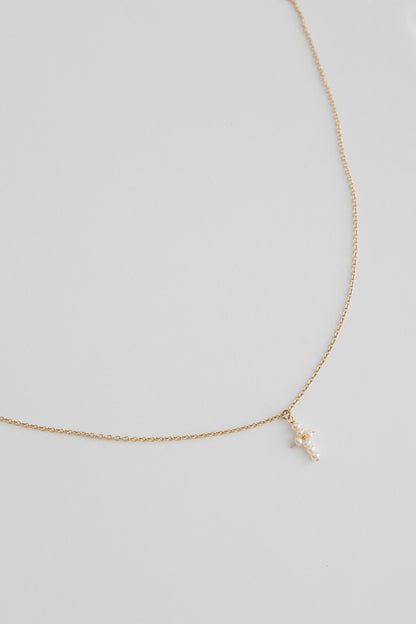 A 14k gold filled cable link chain necklace with freshwater pearls connected in the shape of a cross lays on a white background.