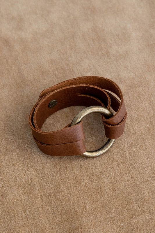 A bronze ring with leather straps connected with a knob button lays on a brown textured background.