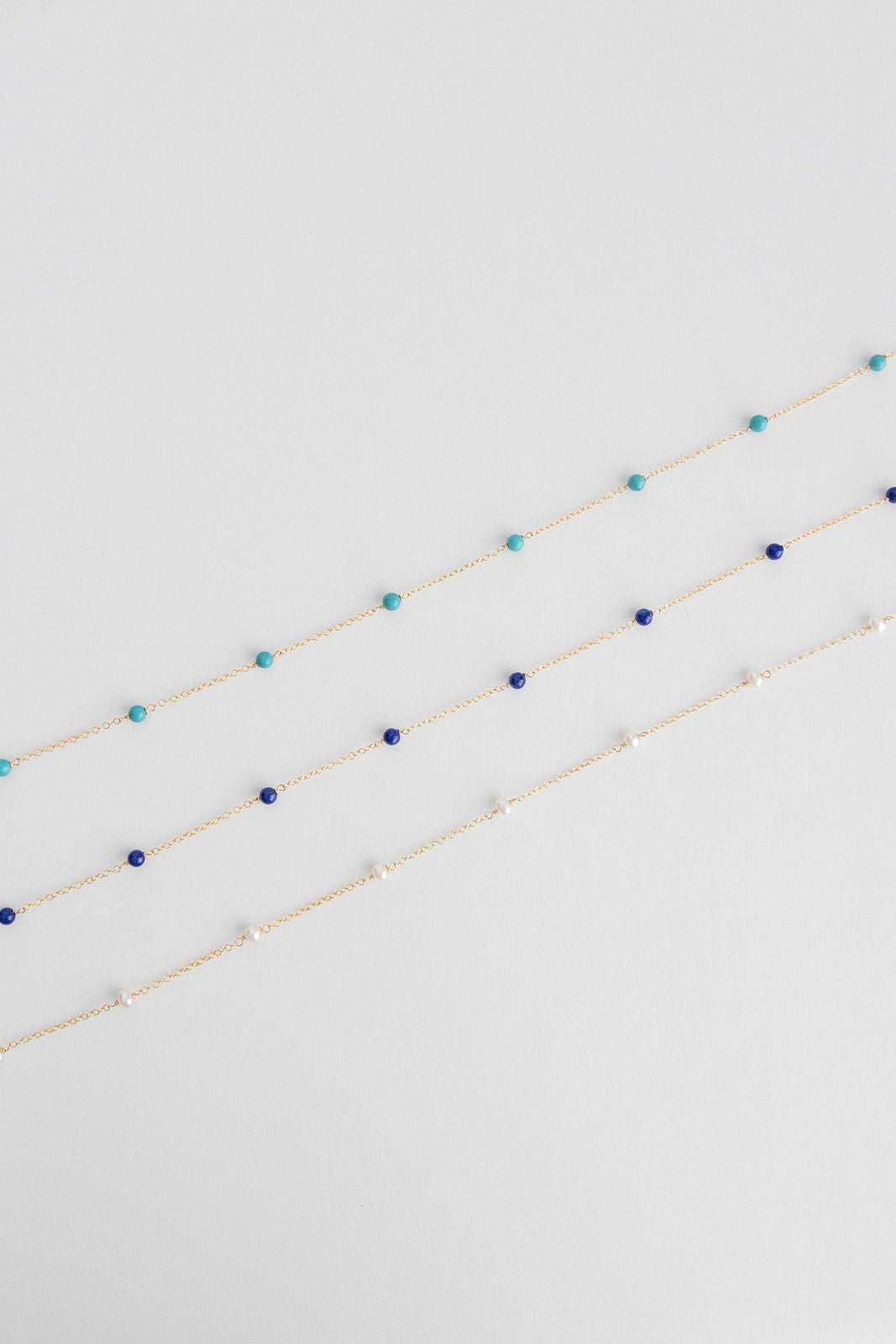 Three necklaces lay on a white background with small freshwater pearls on a 14k gold cable link chain.