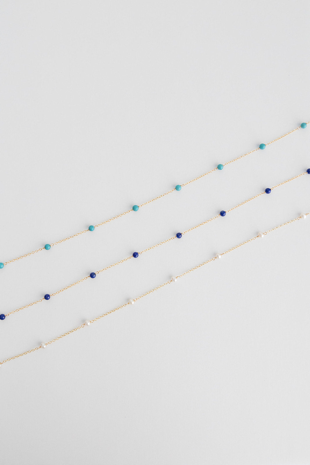 Three necklaces lay on a white background with small freshwater pearls on a 14k gold cable link chain.