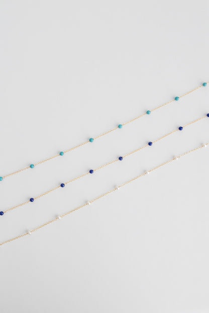 Three necklaces lay on a white background with small freshwater pearls on a 14k gold cable link chain.