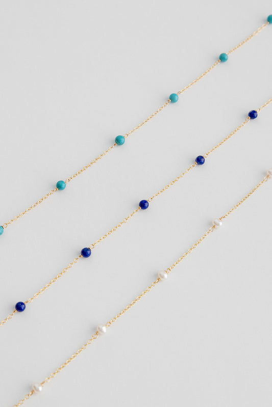 Small freshwater pearls on a 14k gold cable link chain necklace lay on a white background.