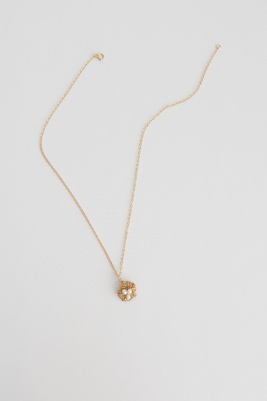 A 14k gold filled wire necklace wrapped to mimic a bird nest with freshwater pearls lays on a white background.