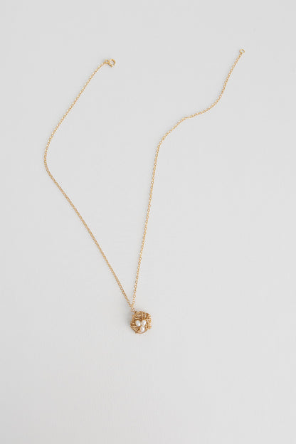 A 14k gold filled wire necklace wrapped to mimic a bird nest with freshwater pearls lays on a white background.