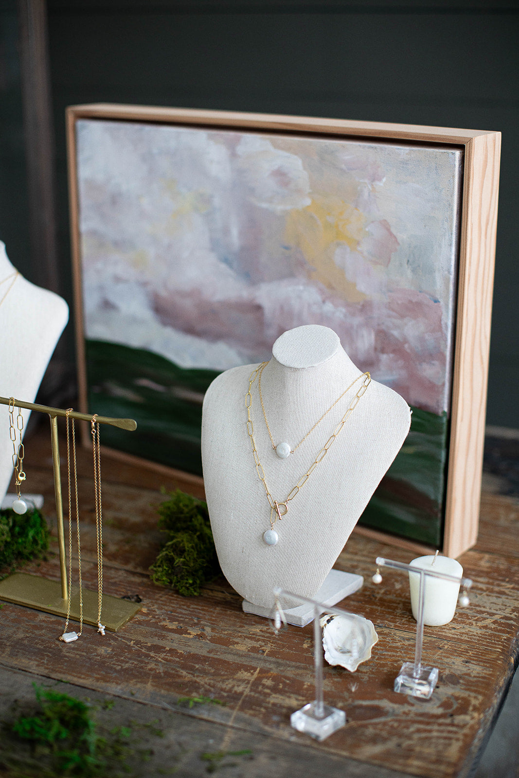A 14k gold filled large paper clip necklace with fresh water coin pearl and toggle lay on a neck jewelry stand paired with another gold necklace.