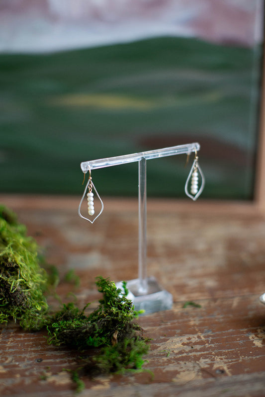 Sterling silver tear drop earrings with five fresh water pearls and 14k gold filled shepherd's hook hang on a clear acrylic earring stand.