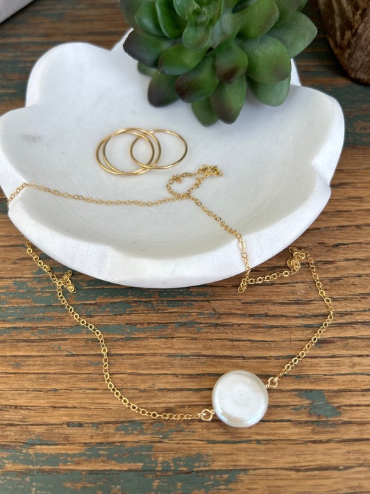 A coin pearl necklace on a 14k gold filled cable link chain drapes over a white ceramic dish on a wood table top.