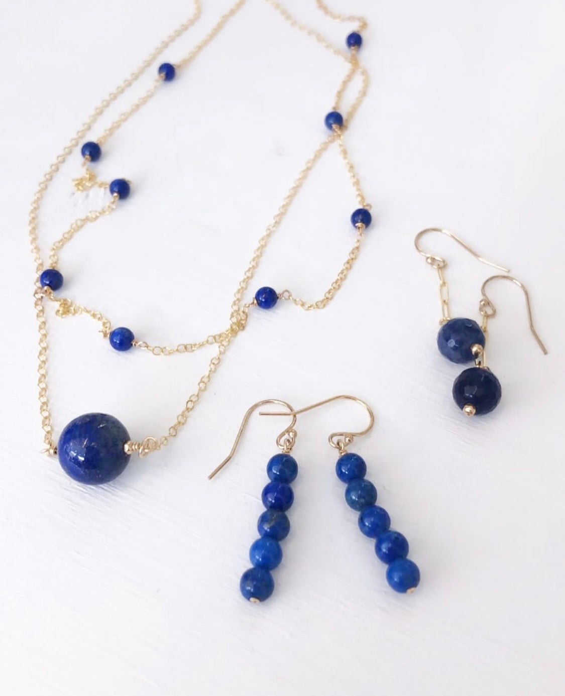 Three 14k gold filled chain necklace with lapis beads lay on a white background.