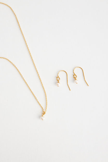 A mini freshwater pearl on a 14k gold filled cable link chain necklace lays next to a pair of matching earrings lays on a white background.