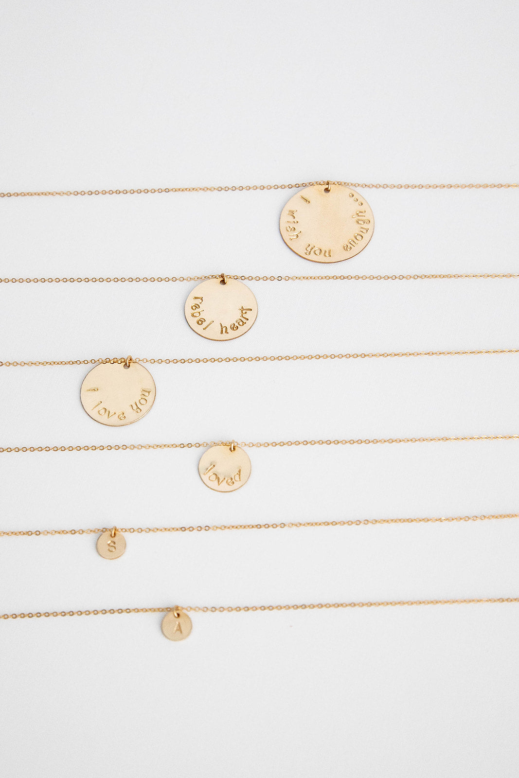 A 25.4 mm 14k gold filled disc hung on a 14k gold cable link chain necklace lays on a white background with more gold necklaces in different sizes.