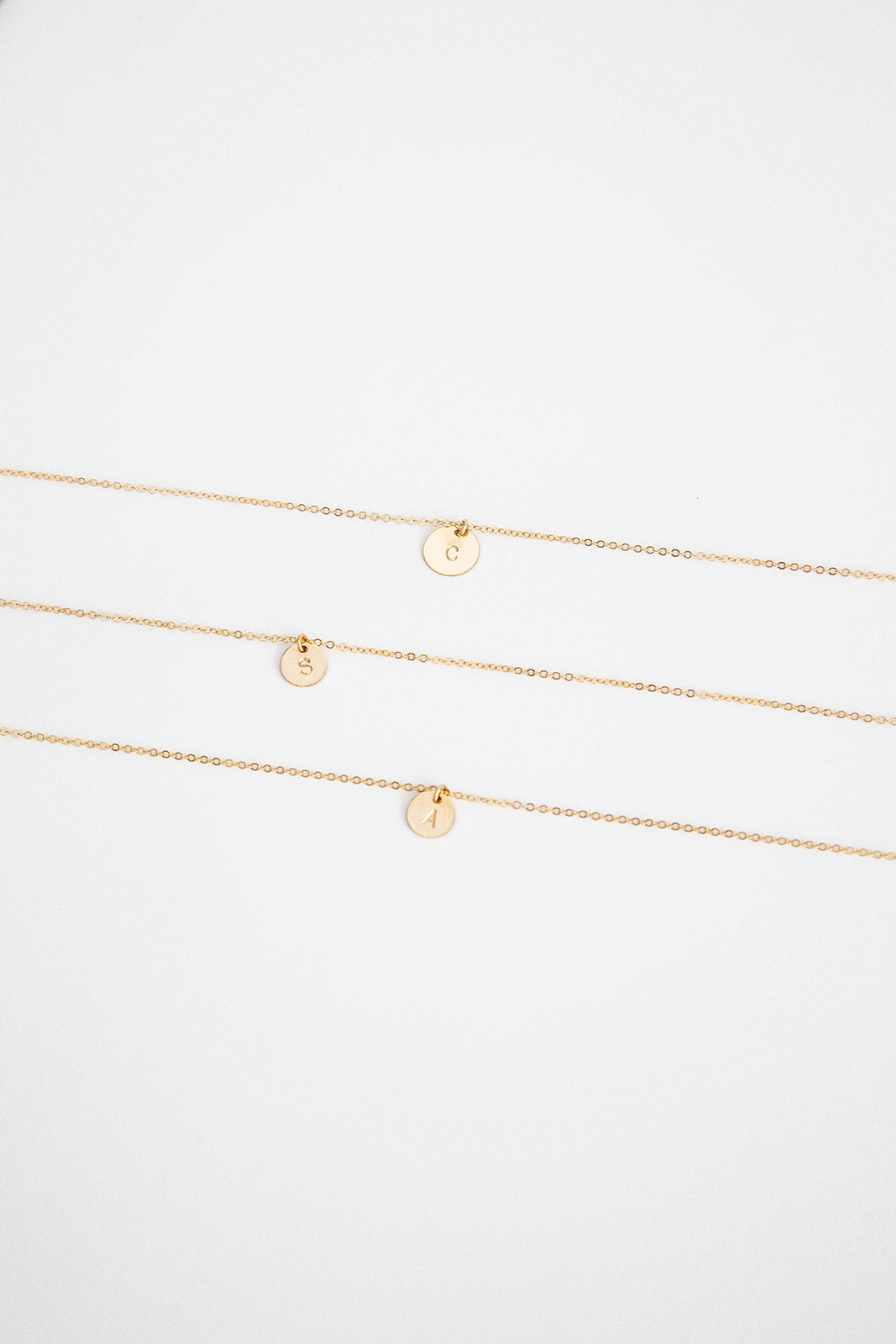 Three 9.5mm 14k gold filled necklaces with hand stamped single letter 14k gold discs lay on a white background.