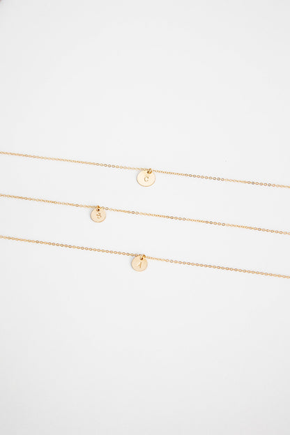 Three 9.5mm 14k gold filled necklaces with hand stamped single letter 14k gold discs lay on a white background.