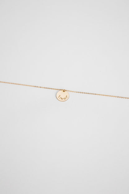 A 14k gold filled disc hung on a 14k gold chain necklace with the word "loved" hand stamped on the disc.