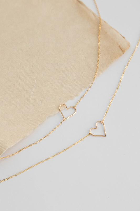 Dainty 14k gold filled floating heart necklace laying on a white background with a beige colored paper.