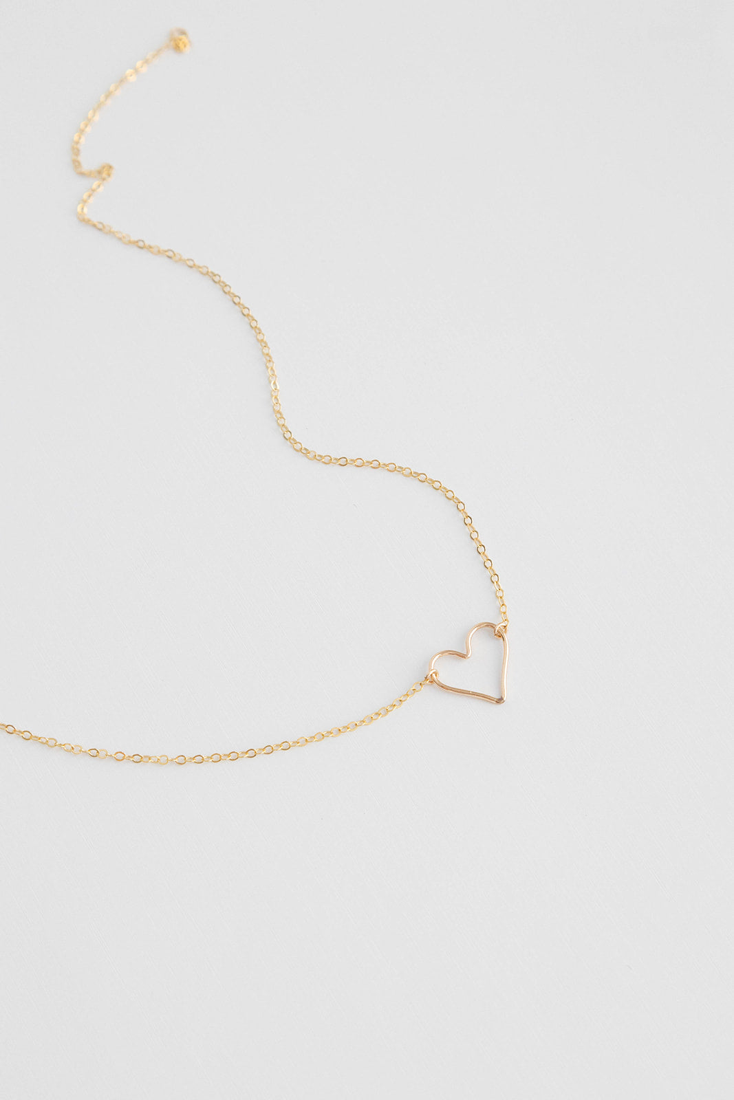 Dainty 14k gold filled floating heart necklace laying on a white background.