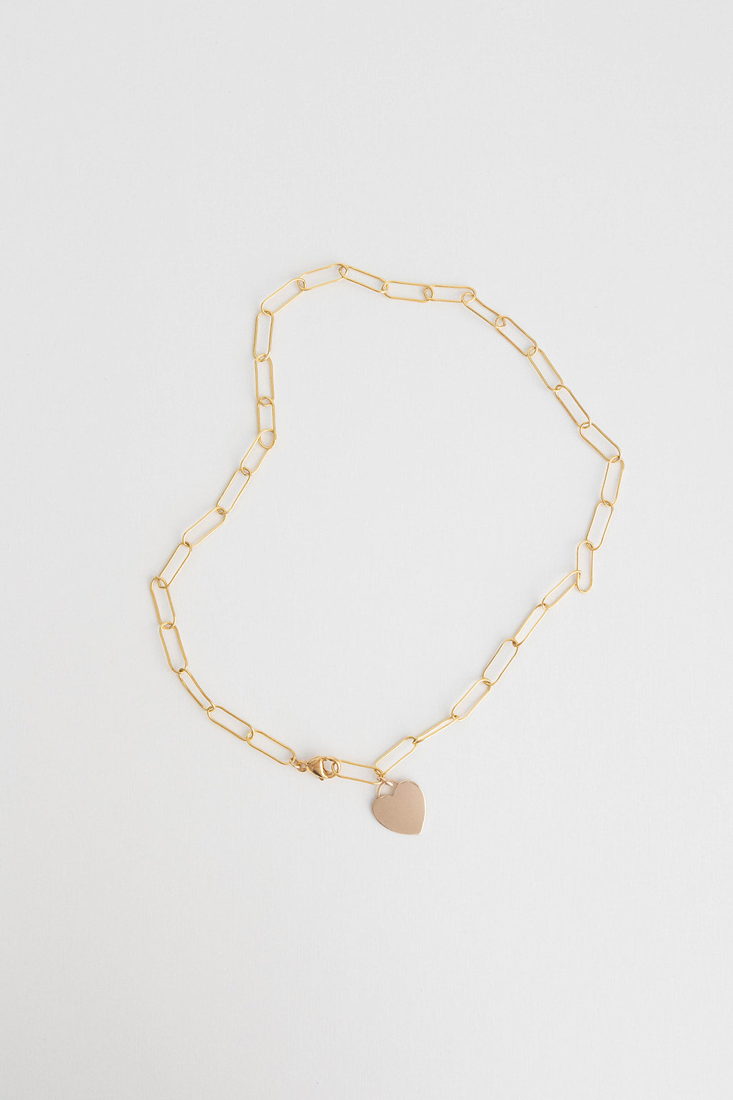 A lightweight 14k gold filled paper clip chain necklace with 14k gold filled heart charm lays on a white background.