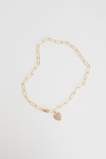 A lightweight 14k gold filled paper clip chain necklace with 14k gold filled heart charm lays on a white background.