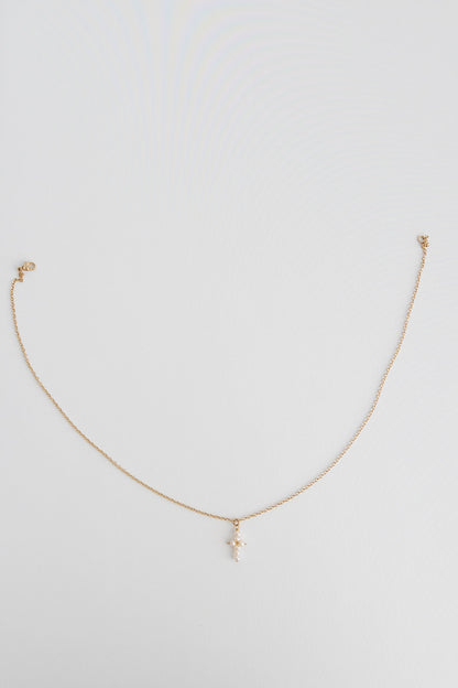 A 14k gold filled cable link chain necklace with freshwater pearls connected in the shape of a cross lays on a white background.