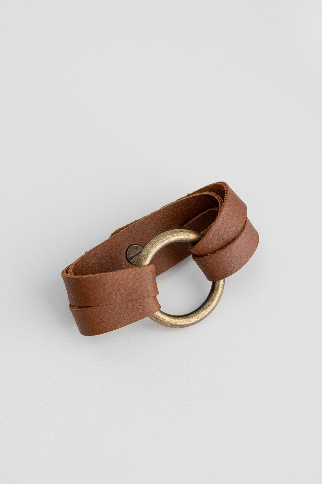 A bronze ring with leather straps connected with a knob button lays on a white background.