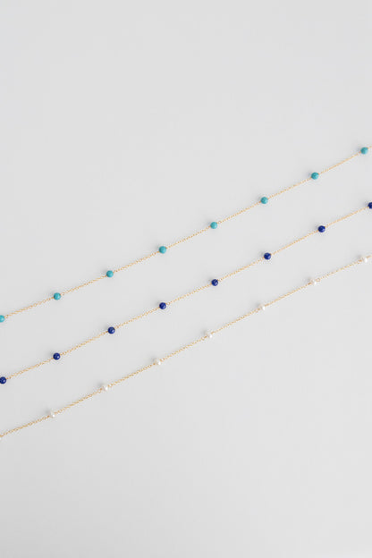 Three 14k gold filled chain necklace with lapis beads lay on a white background.